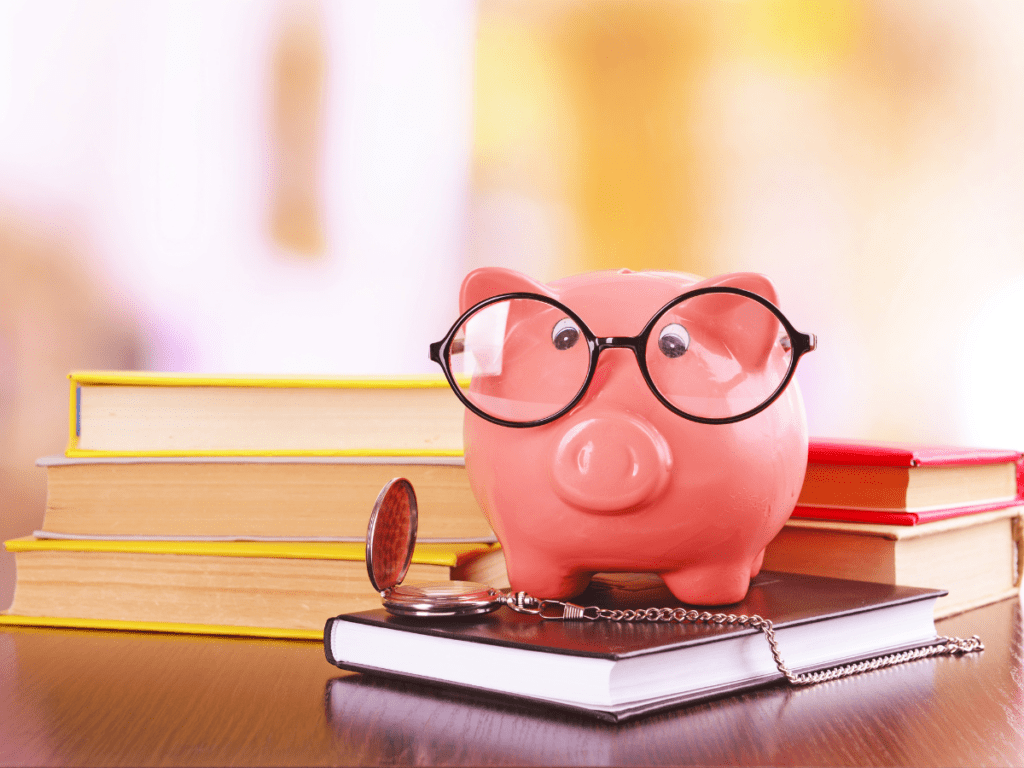 A piggy bank with glasses sitting on top of books