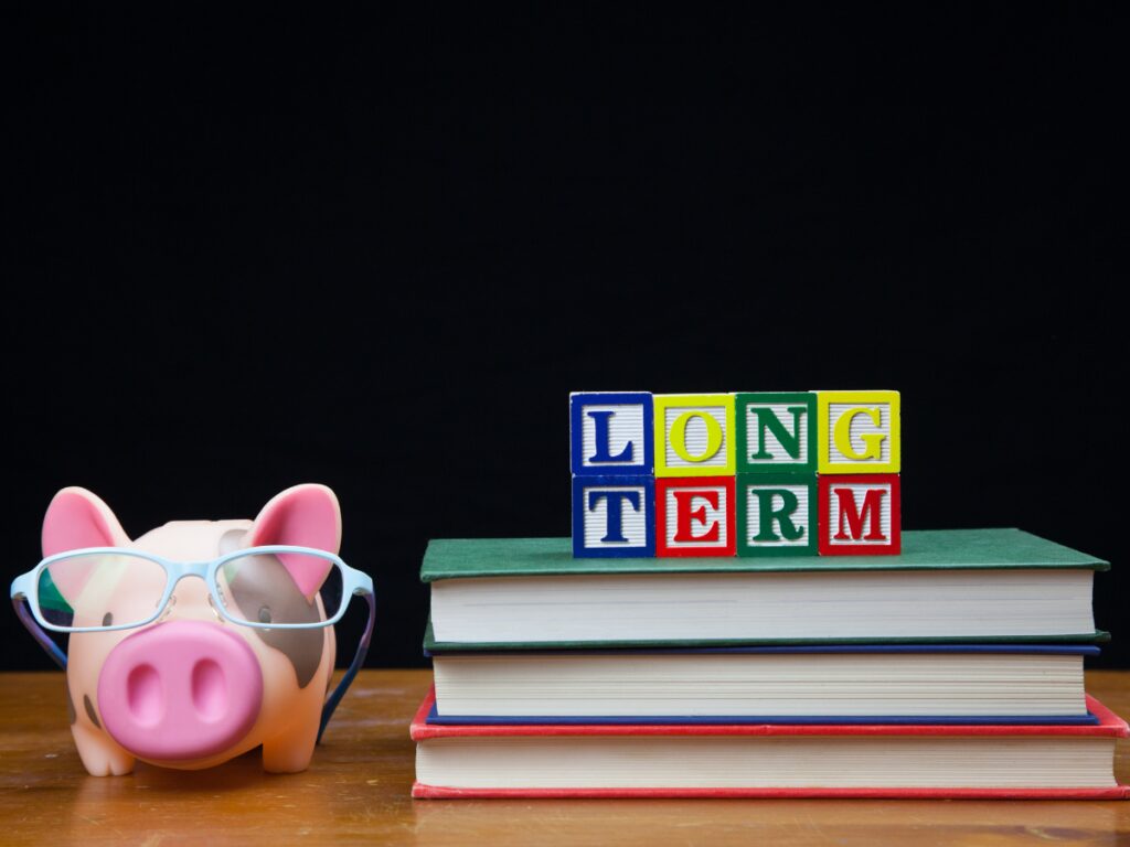 Piggy bank with glasses next to book with words LONG Term